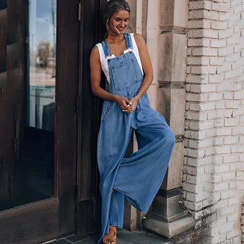 A woman wearing a pair of wide-leg blue denim overalls with pockets, styled with sunglasses and a smile.