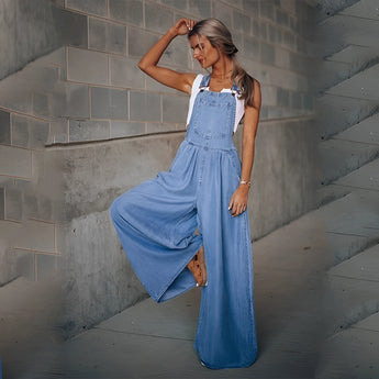 
A woman wearing blue denim wide-leg overalls with pockets, featuring adjustable shoulder straps and a loose fit, standing under flash photography.