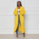 Women's oversized yellow cable knit cardigan sweater worn by a fashion model, showcasing the garment's cozy design with a focus on its long sleeves, collar, and waist.