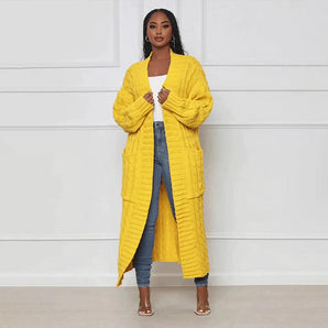 Women's oversized yellow cable knit cardigan sweater worn by a fashion model, showcasing the garment's cozy design with a focus on its long sleeves, collar, and waist.
