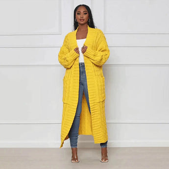 Women's oversized yellow cable knit cardigan sweater worn by a fashion model, showcasing the garment's cozy design with a focus on its long sleeves, collar, and waist.