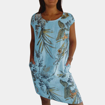 A woman wearing a yellow floral tropical print summer dress with pockets. The dress has a bright design featuring azure and is styled with short sleeves and a fitted waist, showcasing a casual yet elegant summer look.