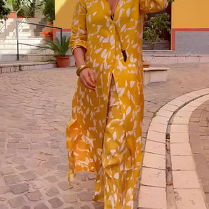 Yellow floral women's loungewear set featuring a long-sleeve pajama design with vibrant orange and yellow floral patterns. The set has a comfortable fit around the waist and sleeves, showcased in a fashion-forward photograph.