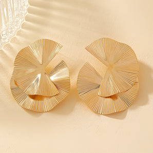 Gold Fan Statement Earrings on wooden table, luxury textured designer jewelry with circular pattern, combining metal and natural materials.