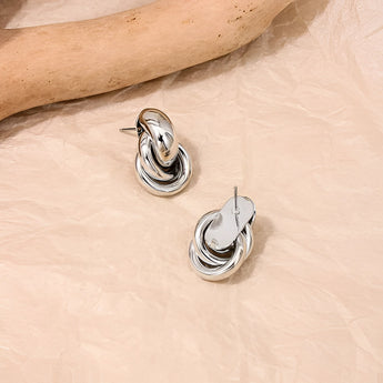 A pair of luxurious, modern silver spiral earrings with multiple loops, designed as high-end body jewelry.