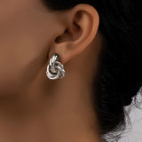 Modern luxury gold spiral earrings with multiple loops, worn on a woman's ear, showcasing designer jewelry.