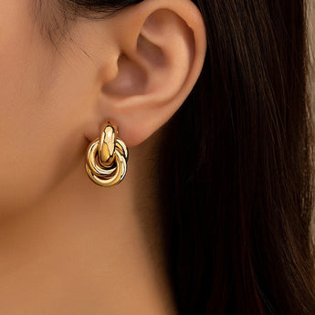 Modern luxury gold spiral earrings with multiple loops, designer jewelry displayed against a wooden background.